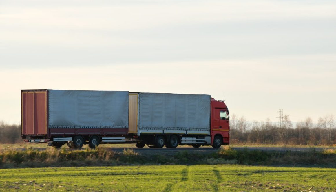 Semi-truck with cargo trailer driving on highway hauling goods in evening. Delivery transportation and logistics concept
